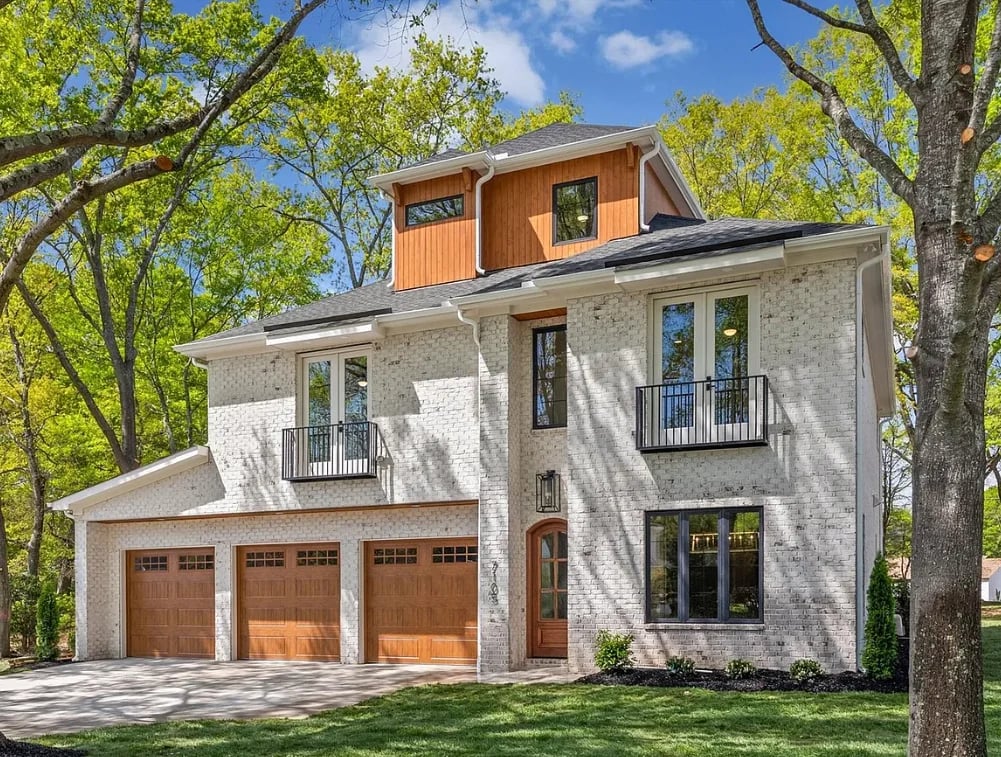 Modern two-story home with brick and white siding, three-car garage, and copper roof cupola surrounded by mature trees